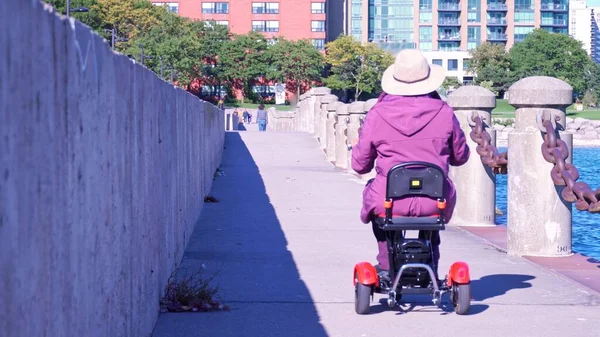 Woman with disability in motorized wheelchair mobility scooter driving around. Recreational electric ability vehicle for people who lives with disability. Accessibility concept.
