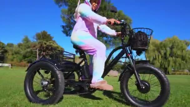 森の公園の晴れた日に電動バイク 電子自転車や自転車に座って愚かなユニコーンのピジャマドレスの旅行者の女性 夏の稲妻だ アクティブな観光 北アメリカの公園での乗り物 — ストック動画