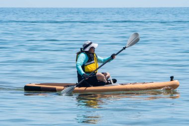 Woman cruising on stand-up paddleboarding SUP. Water sport with paddle at the water. Recreation and fitness. Exploring lake or river while getting a full-body workout. Adventure and sport.