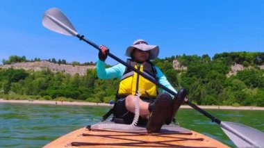 Sportif bir kadın gölde yemek yerken ağır çekimde kürek çekiyor. Ontario Gölü 'nün güzel manzarası, Scarborough Kayalıkları. Aktif yaşam tarzı ve suda spor yapma. Su sporları.