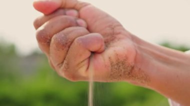 Close-up hand of a woman with handful of sand. Sand from the lake beach spills out on the hot surface of the girls hand. Unrecognizable closeup womans hand playful woman with sand.