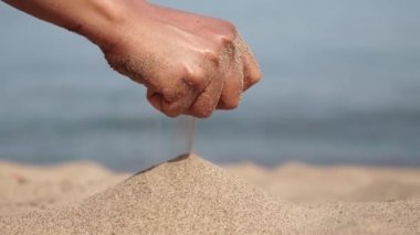 Oyuncu kadının eli bir avuç sarı deniz kumu fırlatıyor. Yaz tatilinde kaygısız kız yumuşak kumlu sıcak ve çarpıcı tropikal plajda oynar. Kadın sıcak kumun parmaklarının arasına düşmesine izin verir..