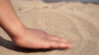Young traveler on a sunny beach in exotic island gently stroking hot sand between her fingertips. Playful woman hand playing with yellow marine sand. Travel, adventure and leisure.