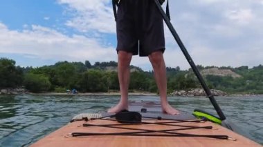 Man standing on SUP and paddling. Stand up paddling surfboard fitness sport. Popular tourist water sport exercising workout on Inflatable stand up paddleboarding, rowing. Recreation and wellness.