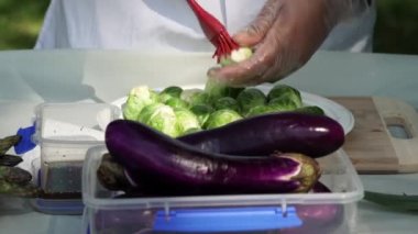 Bahçe pikniği kutlaması hazırlığı. Baharatlı Brüksel lahanası, mangalda ızgara için lahana sebzesi. Beyaz elbiseli kadın aşçı açık havada ızgara yapmak için mangal yapıyor..