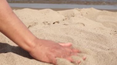 Egzotik adadaki güneşli bir sahilde genç bir gezgin nazikçe parmaklarının arasındaki sıcak kumu okşuyor. Sarı deniz kumuyla oynayan oyuncu kadın eli. Seyahat, macera ve eğlence..