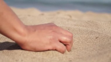Egzotik adadaki güneşli bir sahilde genç bir gezgin nazikçe parmaklarının arasındaki sıcak kumu okşuyor. Sarı deniz kumuyla oynayan oyuncu kadın eli. Seyahat, macera ve eğlence..