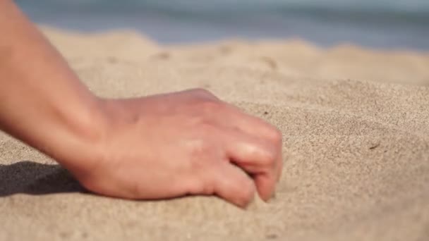 在异国他乡一个阳光普照的海滩上 年轻的旅行者轻轻抚摸着她指尖之间的炽热的沙子 玩世不恭的女人用手玩黄色的海沙 探险和休闲 — 图库视频影像