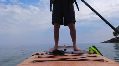 Man standing on SUP and paddling. Stand up paddling surfboard fitness sport. Popular tourist water sport exercising workout on Inflatable stand up paddleboarding, rowing. Recreation and wellness.