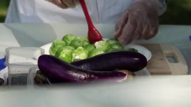 Bahçe pikniği kutlaması hazırlığı. Baharatlı Brüksel lahanası, mangalda ızgara için lahana sebzesi. Beyaz elbiseli kadın aşçı açık havada ızgara yapmak için mangalda mangal yapıyor..