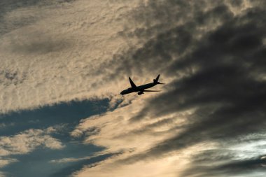 Jet plane small silhouette arrive from travel, sunset evening clouds. Big passenger airplane crossing the sky.