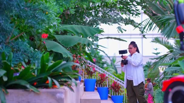在奇异的丛林温室里的女摄影师 半专业的女性旅行摄影师在大自然中散步的时候 在温室热带雨林里拍摄奇异植物的照片 — 图库视频影像