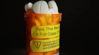 Uyarı etiketli reçeteli ilaç şişesi. Opioidler bağımlılığa, bağımlılığa ve aşırı doza neden olabilir. Bu ilacı bir bardak suyla iç.
