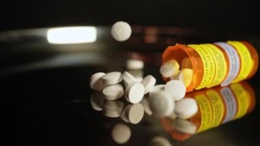 Reçeteli haplar şişeden yavaş çekimde masaya düşer. Farmasötik opioid Amerika 'da ağrı kesici krizi. Uyuşturucu bağımlılığı, aşırı dozda bağımlılığa yol açar. Makro yakın çekim.