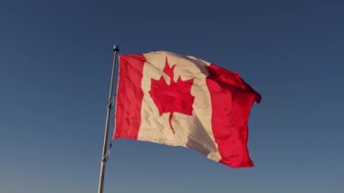 Happy Canadian citizen patriot concept. Canadian flag at wind, blue cloudy sky and golden hour sun.