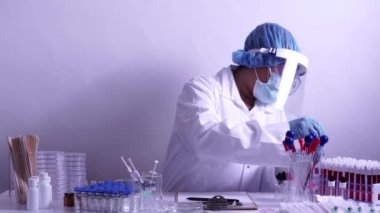 Ekipmanlı tıbbi laboratuvar ve Pediatri önlüğü giyen mikrobiyoloji uzmanı, yüz koruyucu maske takan cam kaplar, çeşitli doku ve kan örnekleriyle çalışıyor. Aşı geliştirmek, uyuşturucu araştırması.
