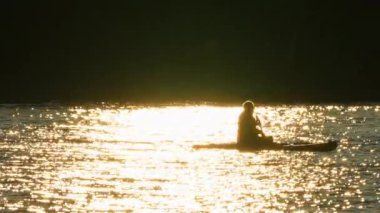 Bir kadının silueti SUP tahtasının üzerinde yüzüyor, altın saat günbatımında kürek çekiyor. Manitou Gölü 'nde hareketli eğlence ve spor için ayağa kalkın. Aktif tatil, meditasyon ve rahatlama.