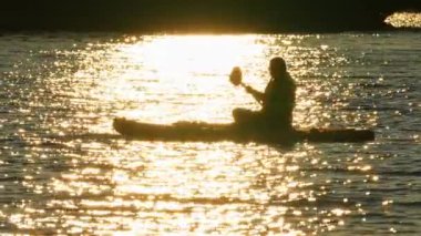 Geleneksel Kuzey Amerika su sporu, bir kadının silueti Kanada 'daki Manitou Gölü' nde SUP tahtasıyla denize açılıyor. Kürek çekme konseptinde yoganın bütünsel sağlığı ve sinerjisi.