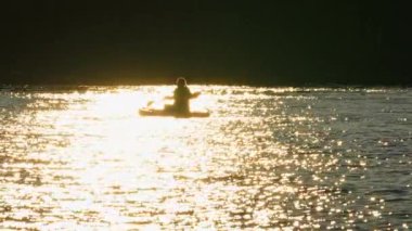Altın saat boyunca Manitou Gölü 'nde yoga yapan bir kadın fiziksel aktivite, zihinsel refah ve doğanın huzuru. Sakin sular ve yüzen SUP ağır çekimde.