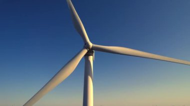 Rüzgar türbininin havada yakın çekim görüntüsü. Rüzgar tarafından dönüyor ve yenilenebilir yeşil enerji üretiyor. Altın saat günbatımında bir rüzgar türbinine yaklaşıyoruz. Enerji alternatifi ve çevre ekolojisi.