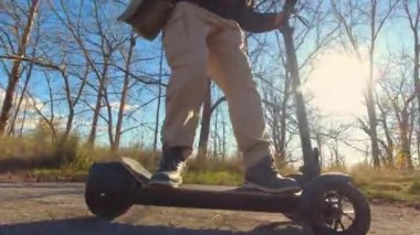 İş ve ayak işleri için şehir parkında elektrikli e-scooter kullanan genç bir adam. Ekoloji ve kolaylık kavramı. Yandan vurulmuş..