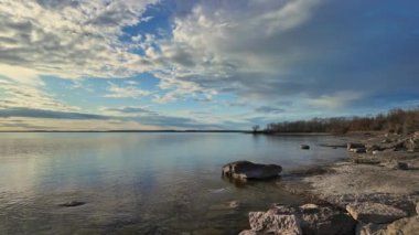Ontario 'daki Prens Edward County Plajı' nda güneş batıyor. Gün batımında Kanada 'da Ontario Gölü' nün suyu sakin. Prens Edward County, Point Petre Sahili düzensiz burnu ya da kireçtaşından yapılmış kireçtaşı kayalıkları.