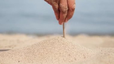Avuç dolusu kumu olan bir kadının eli. Göldeki kumsal, kızların elinin sıcak yüzeyine dökülüyor. Tanımlanamayan yakın plan kadın eli, kumla oynayan oyuncu kadın..
