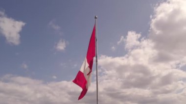 Flag of Canada flying against a summer blue sky. Canadian flag waving on the wind. Canadian flag with maple leaf on the pole slow motion movement.