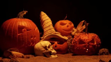 Balkabaklarının Cadılar Bayramı siyah arka planda geçiyor. Cadılar Bayramı ve hasat seti korkuluk ya da cadı şapkası, yabani otlar ve ahır çuvalı üzerinde insan kafatası. Ürkütücü şeytani ve ürkütücü sonbahar süslemeleri.