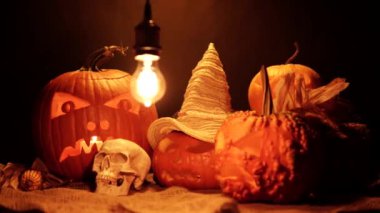 Balkabaklarının Cadılar Bayramı siyah arka planda geçiyor. Cadılar Bayramı ve hasat seti korkuluk ya da cadı şapkası, yabani otlar ve ahır çuvalı üzerinde insan kafatası. Ürkütücü şeytani ve ürkütücü sonbahar süslemeleri.