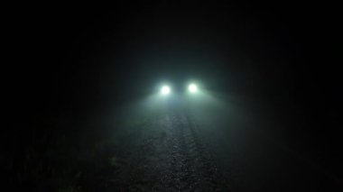 Aracın ön ışıkları şiddetli sis parçacıklarının havada rastgele döndüğünü gösteriyor. Zifiri karanlık yolda dumanlı ve sisli bir gece. Arabanın ışık ve kirişleriyle siyah arkaplan.