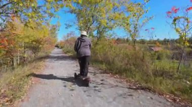 Sonbaharın ortasında gözcülük yaptığı Doube 's Trestle Köprüsü yakınlarındaki Kawartha Trans Canada Trail' de elektrikli e-scooter kullanan bir kadın. Ekoloji ve kolaylık kavramı. Yandan vurulmuş..