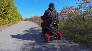 Sonbaharın ortasında Doube 's Trestle Köprüsü' nün yanındaki Kawartha Trans Canada Trail 'de tekerlekli sandalyede scooter kullanan engelli ve hareketli bir kadın. Hareketli Bağımsızlık.