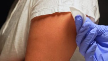 İlaç vermeden önce hastanın omuz derisini temizlemek için pamuk ve alkol kullanan bir sağlık görevlisi. Kadınların el derileri mevsimsel aşılar için dezenfekte edilir..