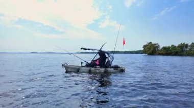 Balıkçı kadın, güneşli yaz günlerinde Kuzey gölünde balık pedalı PDL sürücüsü kanosunda kanoyla kürek çekiyor. Kano balıkçılığı yaz sporları. Gölde çubuklarla kano süren bir kadın balık yakalıyor..