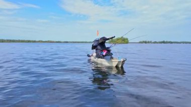 Gölde çubuklarla kano süren bir kadın, balık tutuyor. Balıkçı kadın güneşli yaz gününde gölde balık pedalı PDL kayığında kano tutuyor ve kano tutuyor. Kano balıkçılığı yaz sporları.