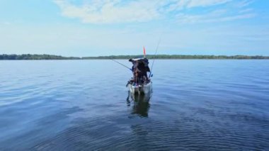 Gölde balık tutan balıkçı kanocu. Angler, Kanada 'da gölün ortasında kanoya oyuncu seçip sersemletiyor. Mavi gökyüzü ve bulutlar arka plan.