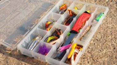 Ahşap kaya yüzeyinde yapay balıkçı teçhizatı bulunan olta çantası. Balık seçici odaklanma için aksesuarları yakından çek. Crankbait üç kat yem ya da kaşık, jig spinner, yumuşak plastik ve yüzme yemi