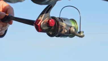 Kuzey Amerika 'daki gölde balık avlayan tanınmayan bir kadına yakın çekim. Kadınlar olta kamışı tutarken, örgü örerek sığ bir odak tutarlar. Balıkçı kadın oltanın makarasını çeviriyor..