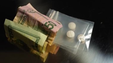 Uyuşturucu ticareti konsepti, uyuşturucu krizi ve yasadışı işlemler. Uyuşturucu satıcısı tarafından paketlenmiş naylon torbada reçeteli opioid oksi hapları. Metalik yüzeyinde buruşuk Amerikan doları banknotları var. Kirli para