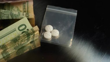 Uyuşturucu ticareti konsepti, uyuşturucu krizi ve yasadışı işlemler. Uyuşturucu satıcısı tarafından paketlenmiş naylon torbada reçeteli opioid oksi hapları. Metalik yüzeyinde buruşuk Amerikan doları banknotları var. Kirli para
