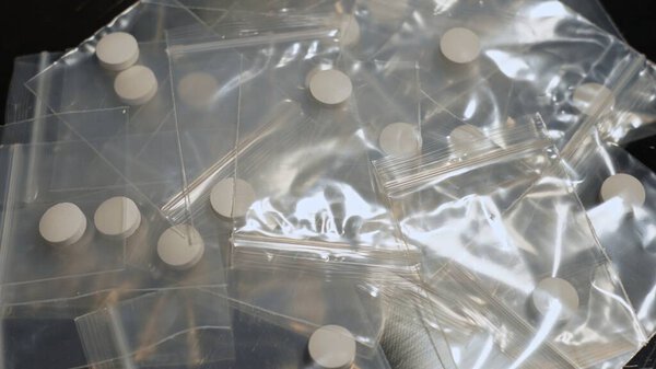 Таблица наркоторговцев с таблетками фентанила в прессованной пудре, упакованной в маленькую сумку, героин и метамфетамины, незаконные наркотики. Опасный фентанил и денежные счета улик на месте преступления.