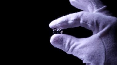 Beyaz eldivenli kuyumcu elleri büyüteçle parıldayan elmasın kalitesini inceler. Seçici odaklanma, makro. Kalite denetimi. Nişan ya da alyans için yuvarlak elmas..