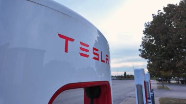 Tesla, Kanadalı bir lastik dükkanının dışındaki geniş bir otoparkta şarj ediyor. Kentsel bir ortamda modern elektrikli araç altyapısı: Toronto, Ontario, Kanada - 20 Eylül 2024
