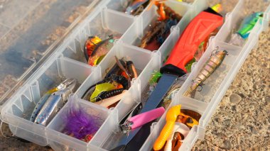Kaya yüzeyinde yapay balıkçı teçhizatı olan bir olta kutusu. Balık seçici odaklanma için aksesuarları yakından çek. Crankbait üç kat yem ya da kaşık, jig spinner, yumuşak plastik ve yüzme yemi