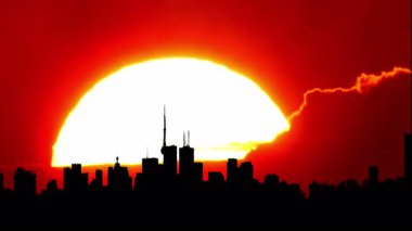 Şehrin ufuk çizgisi silueti, sıcak sinematik güneş batımı, şehir merkezi, büyük güneş batımı ışığı olan şehir merkezi. Sanatsal efektler. Binalar ve sarı güneş diskleriyle destansı sıcak yaz gökyüzü. Isı dalgası uyarısı.