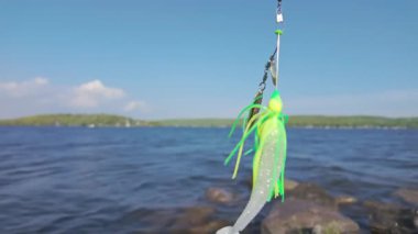 Pike ya da Bass balıkçılığı, seçici olarak yakın çekim odağı sağlar. Kaşık ve yumuşak plastik kürek kuyruğuyla dönen yem rüzgarda bulanık göle ve mavi gökyüzüne doğru hareket ediyor. Yapay Balık Yemi.