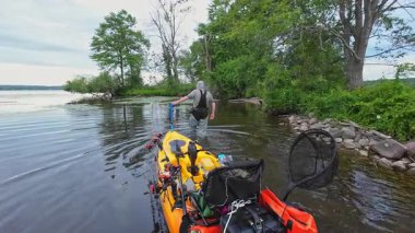 Balıkçı kanosunu ya da su aracını fren için göl kıyısına çekiyor. Sakin göl sularında kano balıkçılığı ve huzurlu manzaralar. Su sporu levreği ve balık avı.