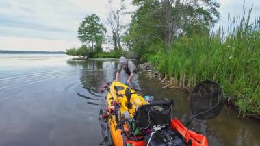 Balıkçı kanosunu ya da su aracını fren için göl kıyısına çekiyor. Sakin göl sularında kano balıkçılığı ve huzurlu manzaralar. Su sporu levreği ve balık avı.