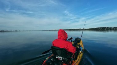 Bir kayıkta oturan balıkçı, elinde kürek tutarken balık yakalamak için gizli bir yere gidiyor. Kano balıkçılığı yarışması. Çevre koruma ve soğuk su için kuru giysili balıkçı..